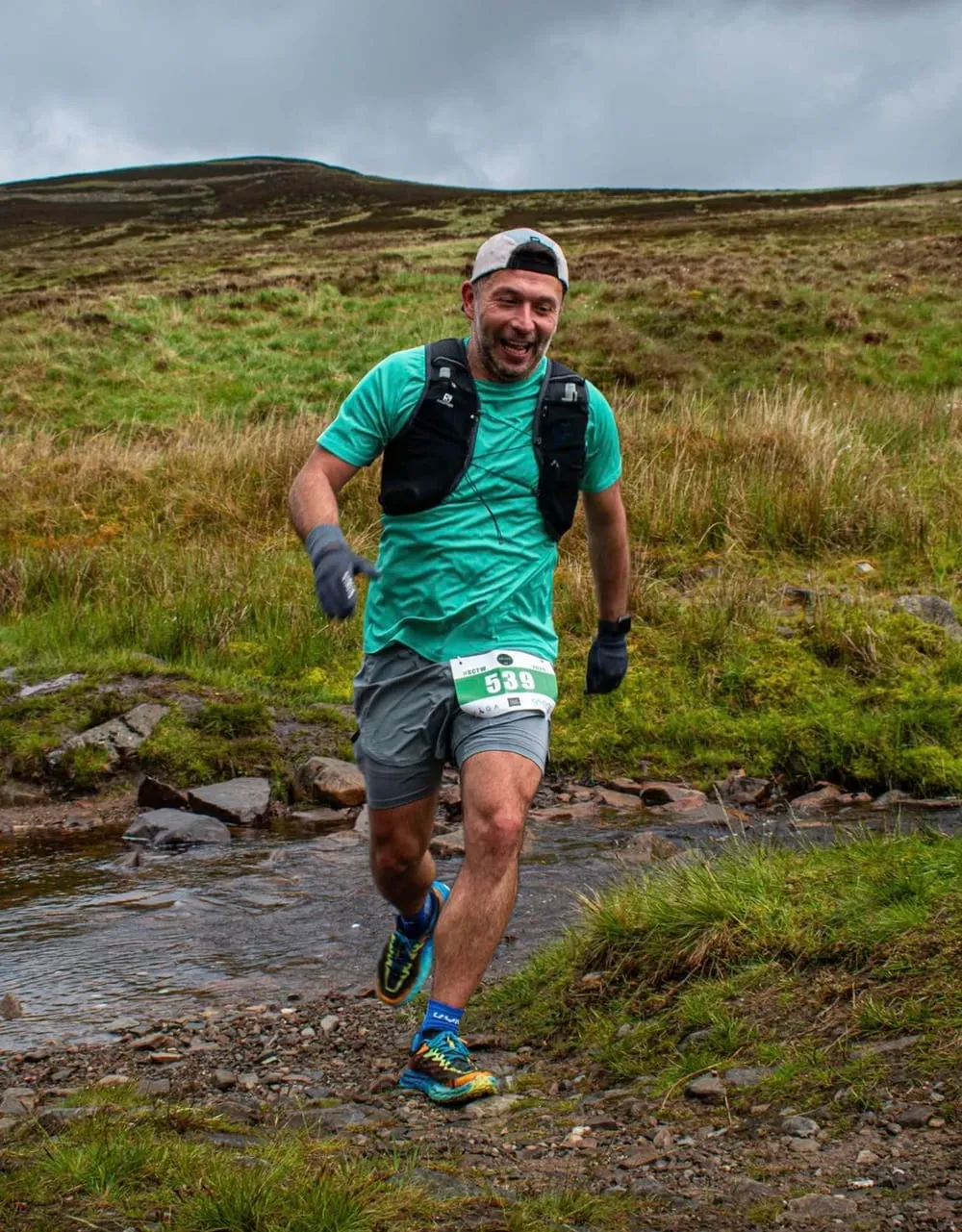 Michal running a trail race across a stream in the hills